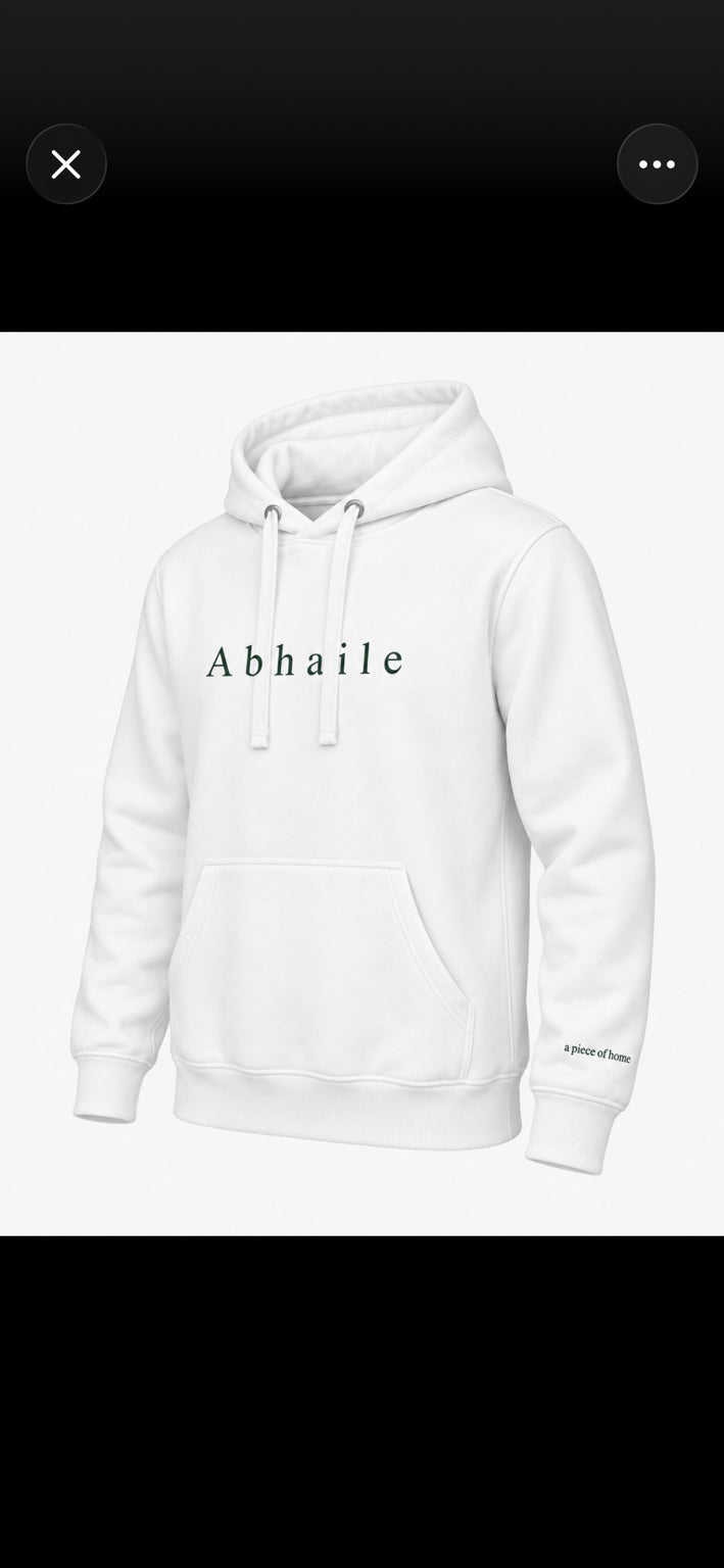 Design mockup of the white Abhaile hoodie with green chest lettering and sleeve detail; final product photography to follow.